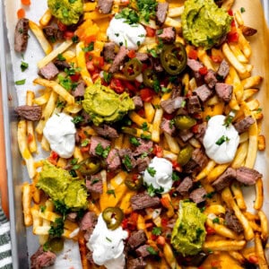 Baking tray topped with carne asada fries loaded with meat, cheese, guacamole, jalapeños, pico de Gallo, and sour cream.