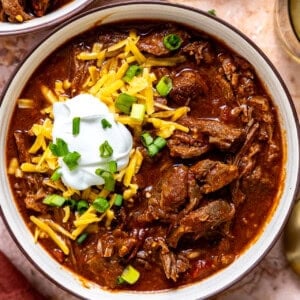 A bowl of hearty chuck roast chili topped with shredded cheese, sour cream, and chopped green onions.