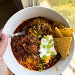 Homemade bowl of chuck roast chili topped with sour cream, cheese, and tortilla chips on the side. 