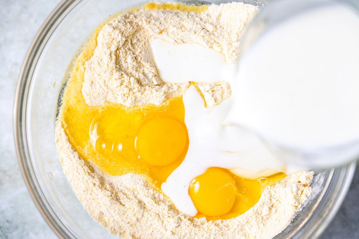 Dry ingredients in a bowl with eggs and buttermilk being poured in, ready to be mixed for spicy cornbread.