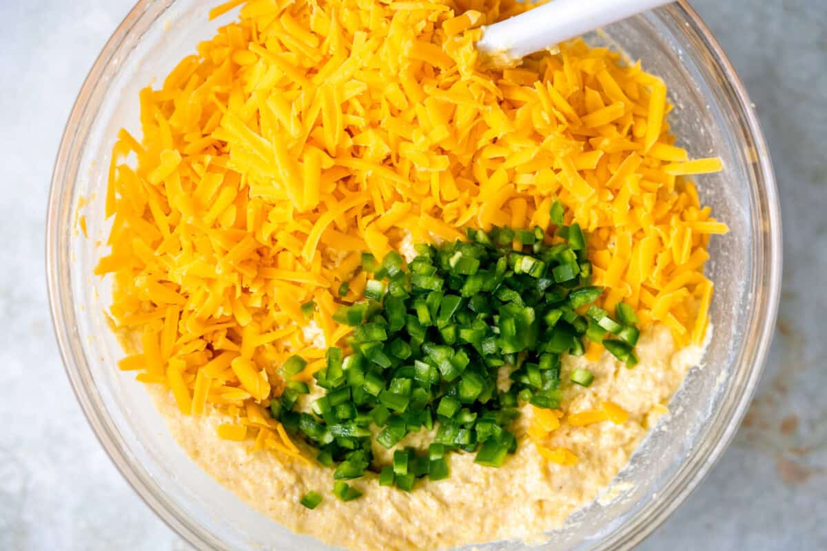 Grated cheddar cheese and fresh diced jalapeno being added to cornbread batter. 