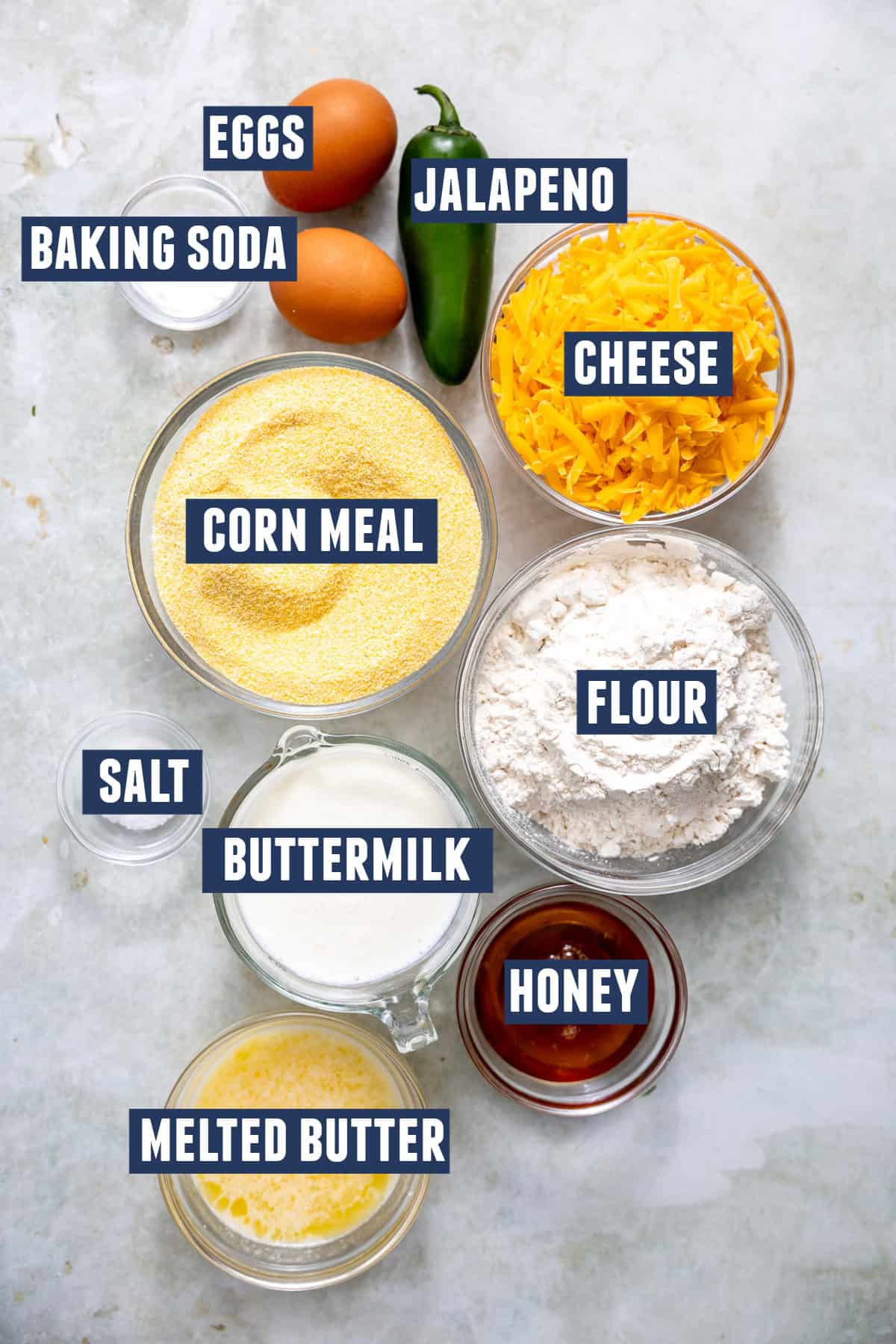 All ingredients for jalapeño cheddar cornbread arranged on a countertop, including fresh jalapeños, cheddar cheese, cornmeal, eggs, milk, flour, and butter.