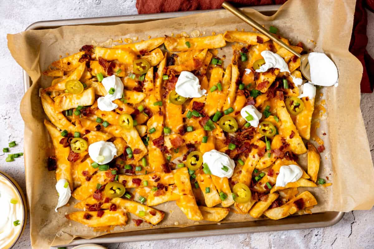 Dollops of sour cream on a tray of loaded cheese French fries. 