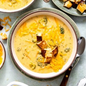 A creamy bowl of broccoli cheddar soup topped with shredded cheddar cheese and served with a side of crusty bread.