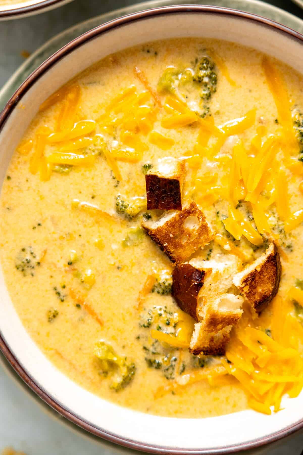 Bowl of creamy broccoli cheddar soup topped with crunchy bread croutons and extra cheese. 