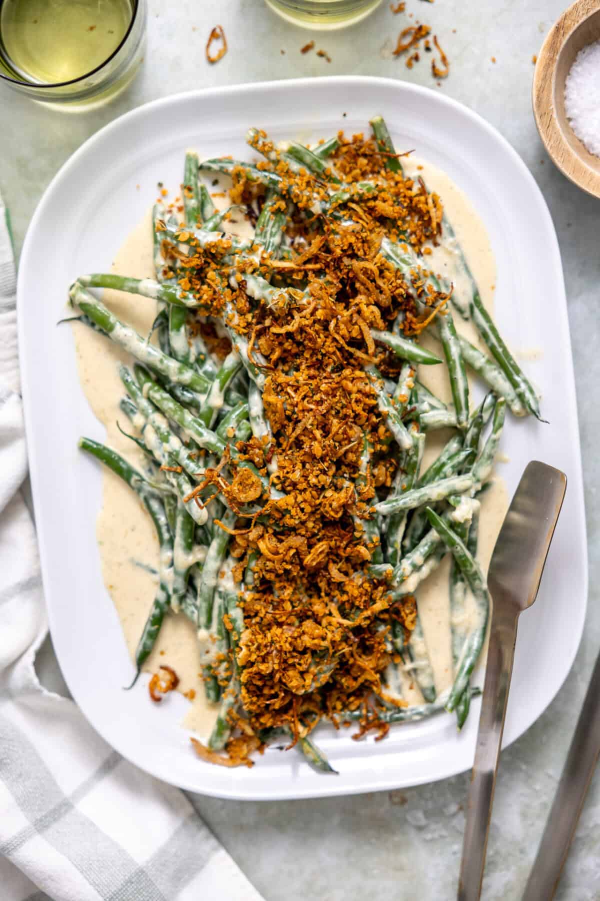 Creamed green beans on a white dish topped with a shallot herb crispy topping. 