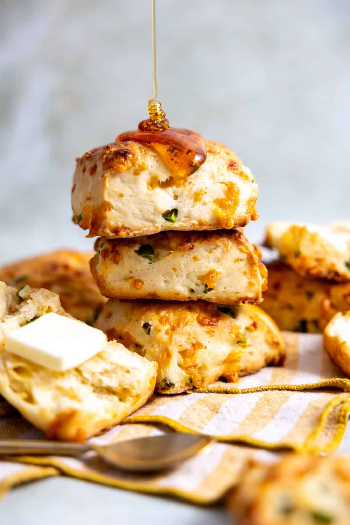 Stack of jalapeño cheddar biscuits being drizzled with honey and served with butter. 