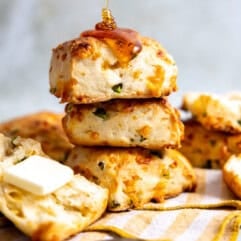 Stack of jalapeño cheddar biscuits being drizzled with honey and served with butter.