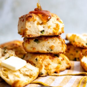 Stack of jalapeño cheddar biscuits being drizzled with honey and served with butter.