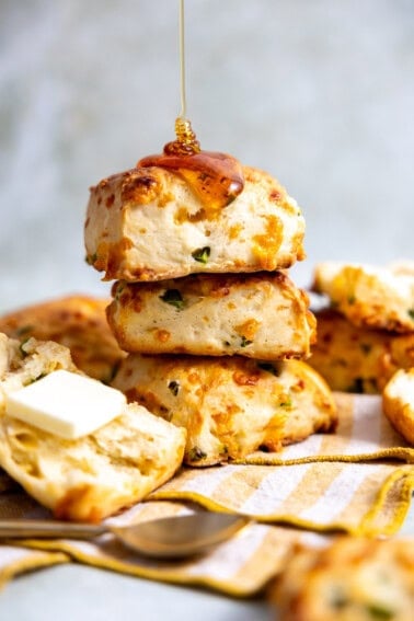 Stack of jalapeño cheddar biscuits being drizzled with honey and served with butter.