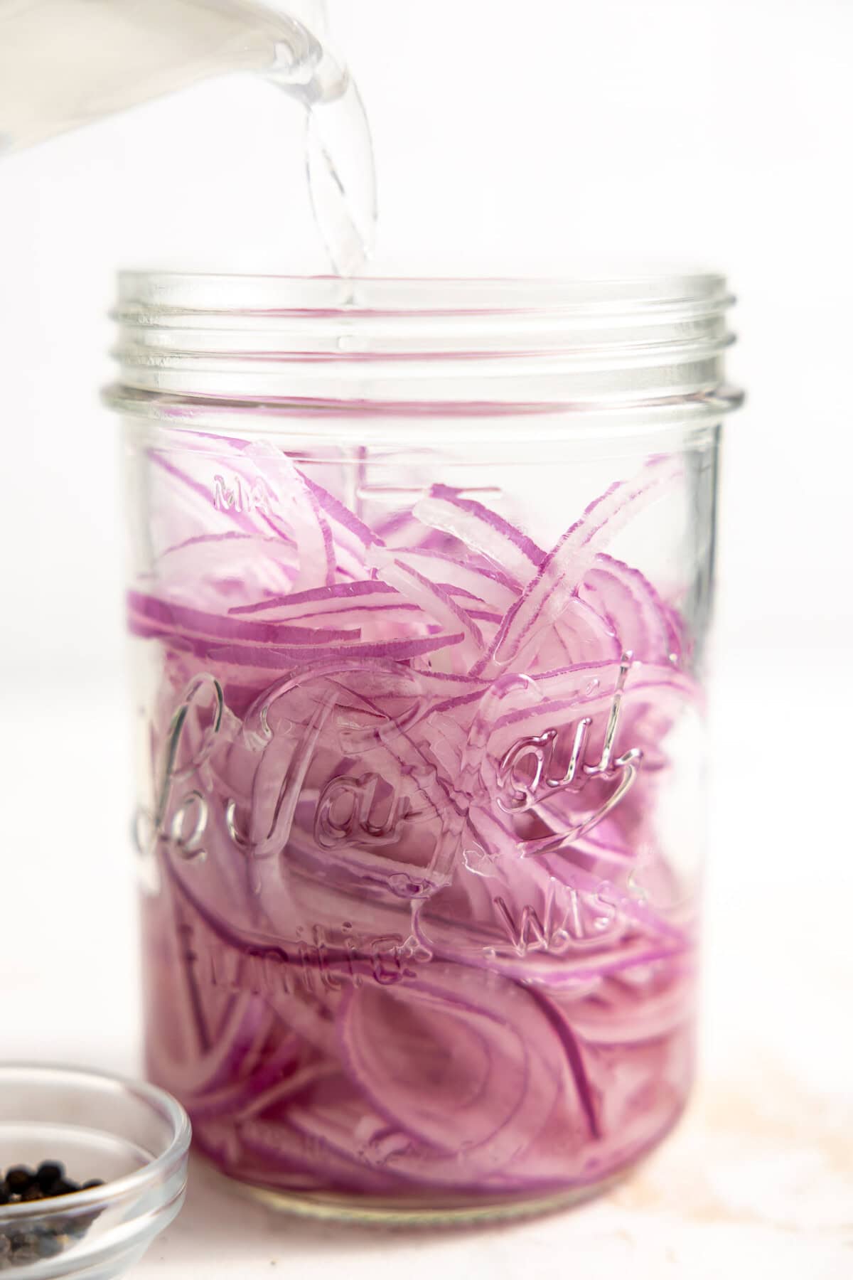 Pouring vinegar over thinly sliced red onions in a jar to make easy pickled onions. 