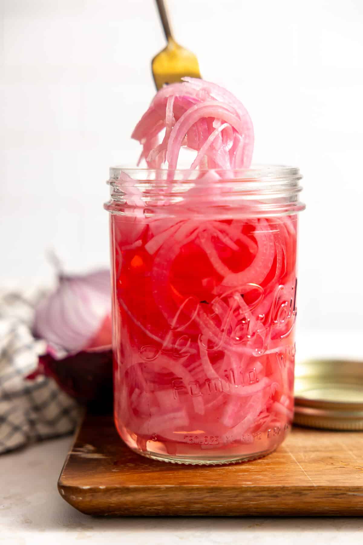 A jar filled with tangy and sweet pickled red onion being served up with a fork. 