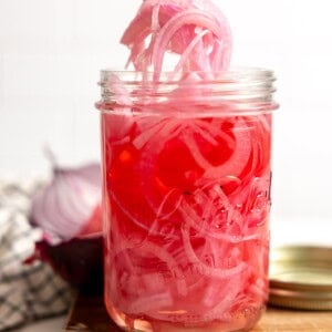 A jar filled with tangy and sweet pickled red onion being served up with a fork.