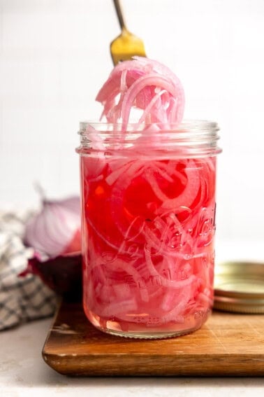 A jar filled with tangy and sweet pickled red onion being served up with a fork.