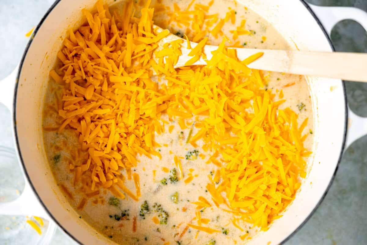 Cheddar cheese being stirred into a pot of broccoli soup. 