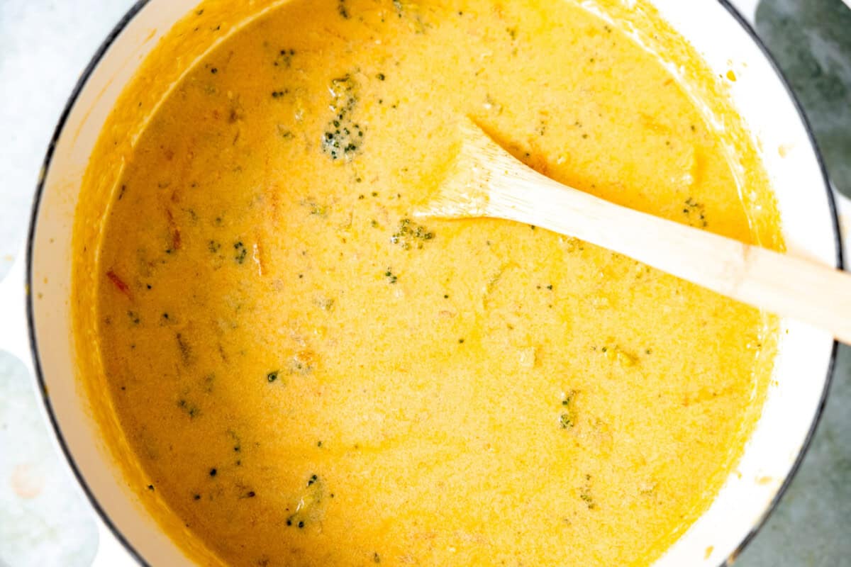 A full pot of broccoli cheddar soup with a spoon for serving. 