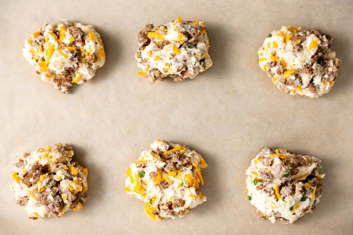 Cheese and sausage biscuit dough dropped on a sheet pan for baking.