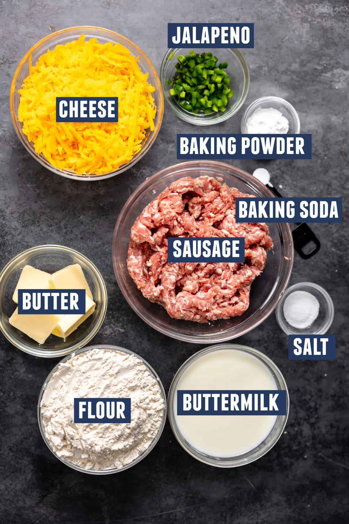 Ingredients needed to make cheese and sausage biscuits including: flour, sausage, cheese, jalapeno, baking powder, baking soda, salt, buttermilk, and butter. 