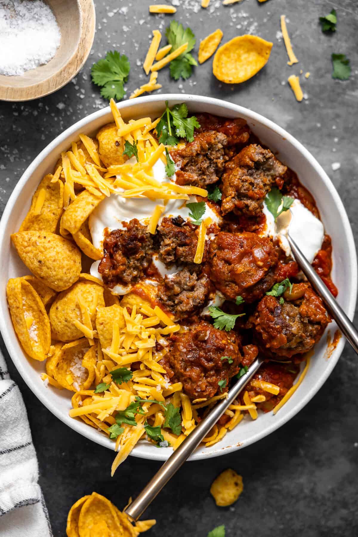 Bowl of meatball chili served with Fritos, grated cheese, and sour cream.