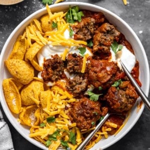 Bowl of meatball chili served with Fritos, grated cheese, and sour cream.