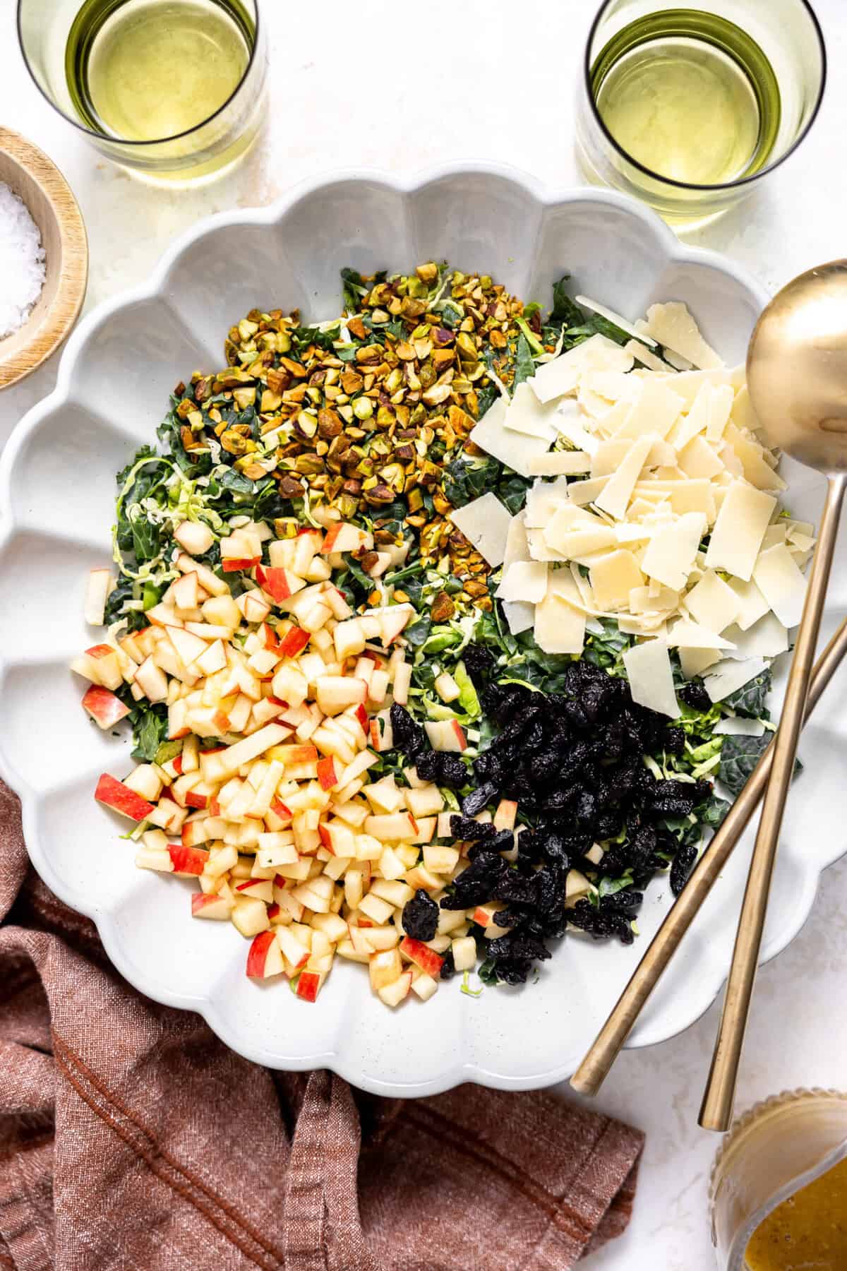 Kale and brussels sprout salad topped with apple, pistachios, dried cherries and parmesan in a white serving bowl. 