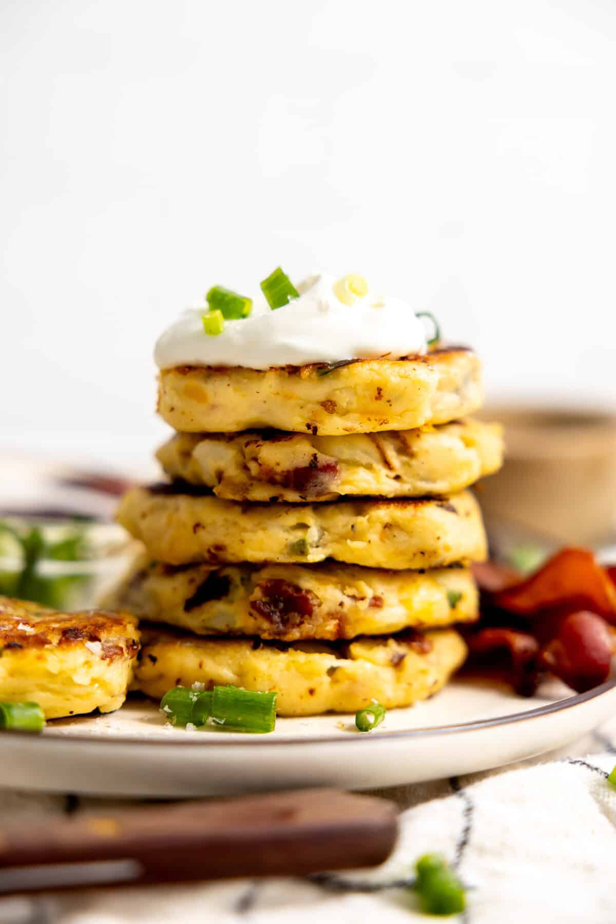 Stack of mashed potato cakes topped with sour cream and sliced green onion.