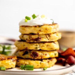 Stack of mashed potato cakes topped with sour cream and sliced green onion.