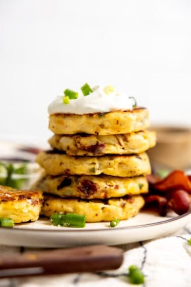 Stack of mashed potato cakes topped with sour cream and sliced green onion.