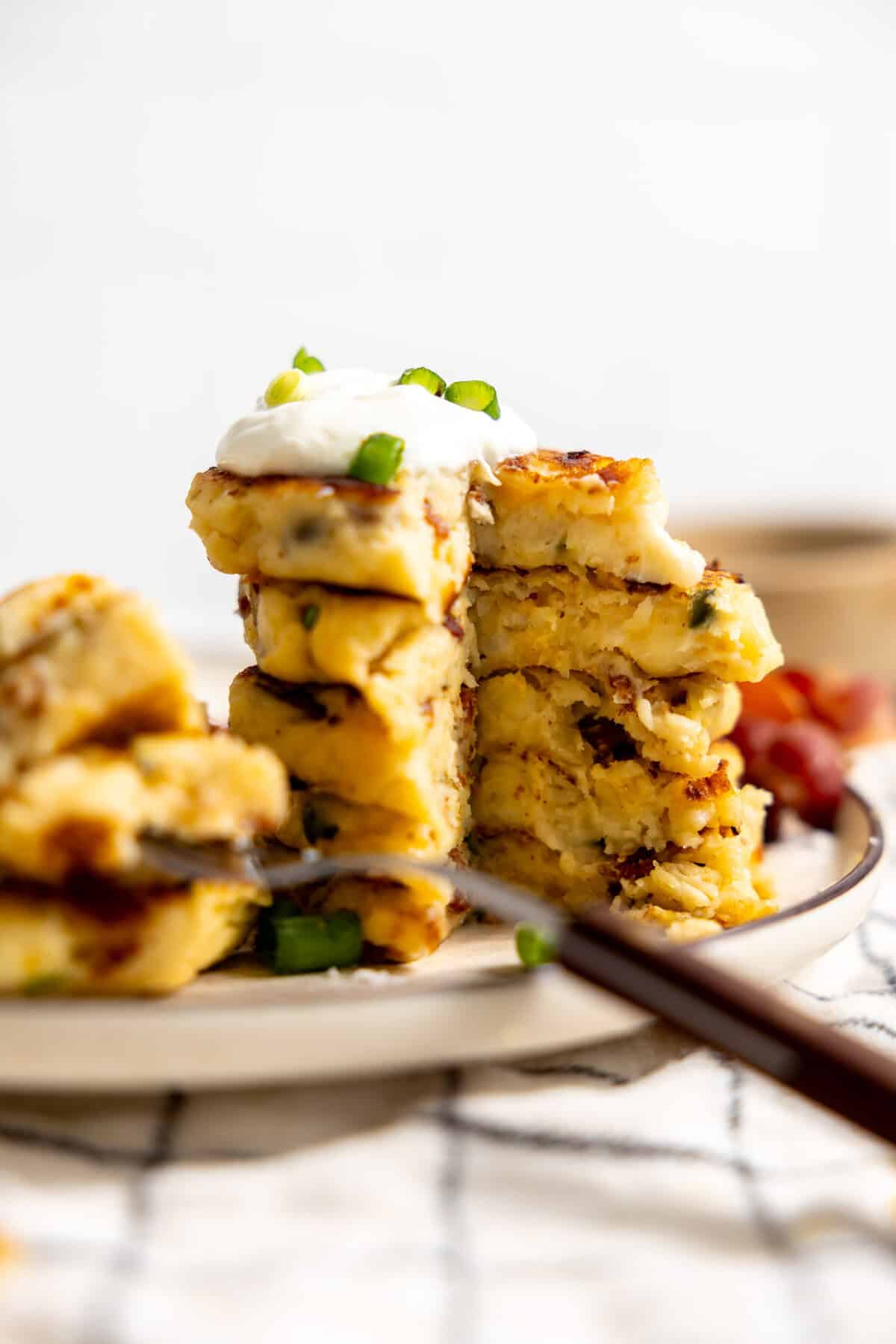 Stack of mashed potato cakes topped with sour cream, with a slice taken out of the stack. 