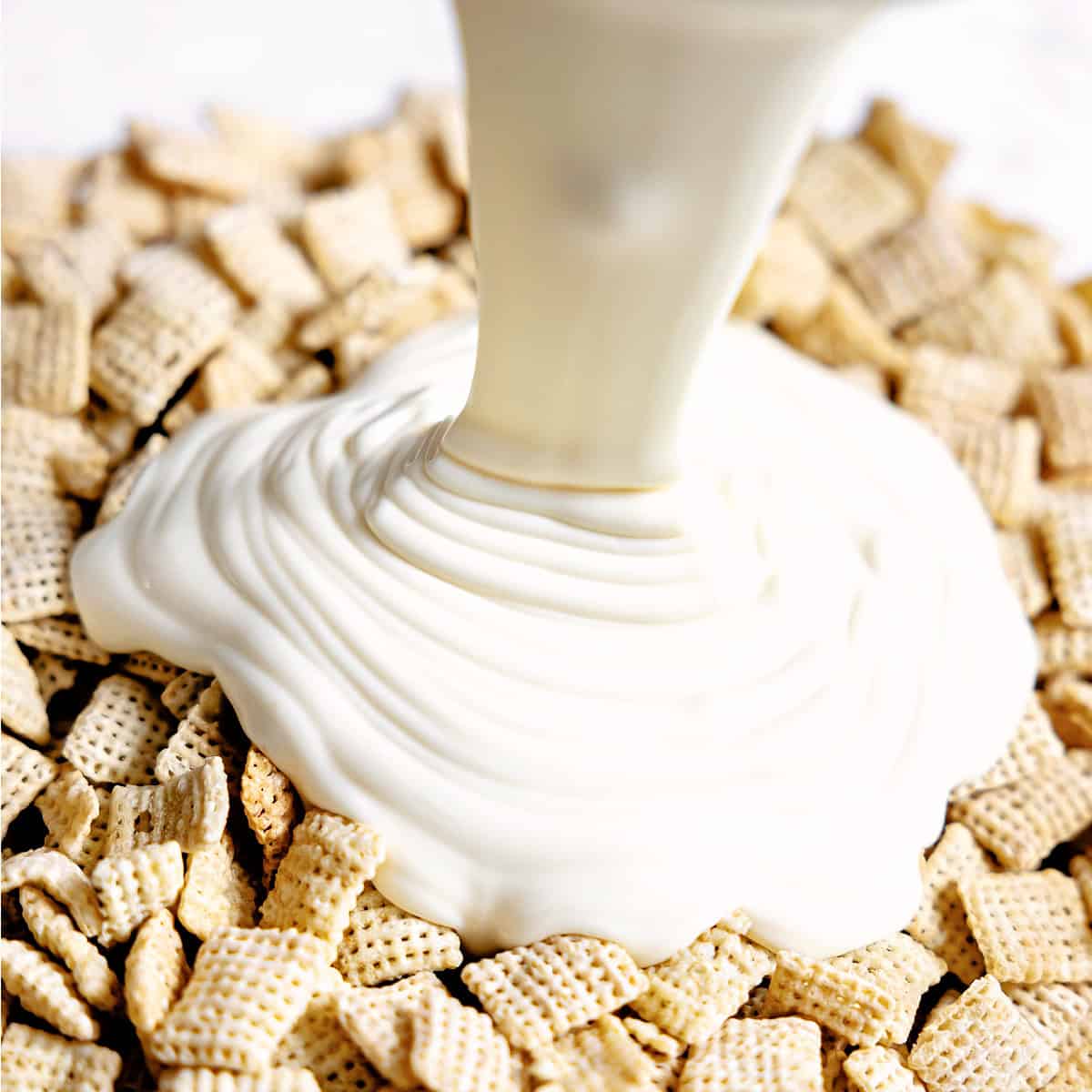 White chocolate being poured over rice Chex cereal. 