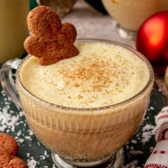 Eggnog latte served in a glass mug topped with cream, a sprinkle of nutmeg, and a gingerbread man cookie.