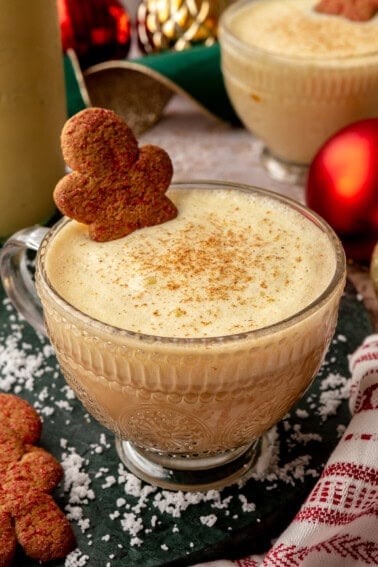 Eggnog latte served in a glass mug topped with cream, a sprinkle of nutmeg, and a gingerbread man cookie.