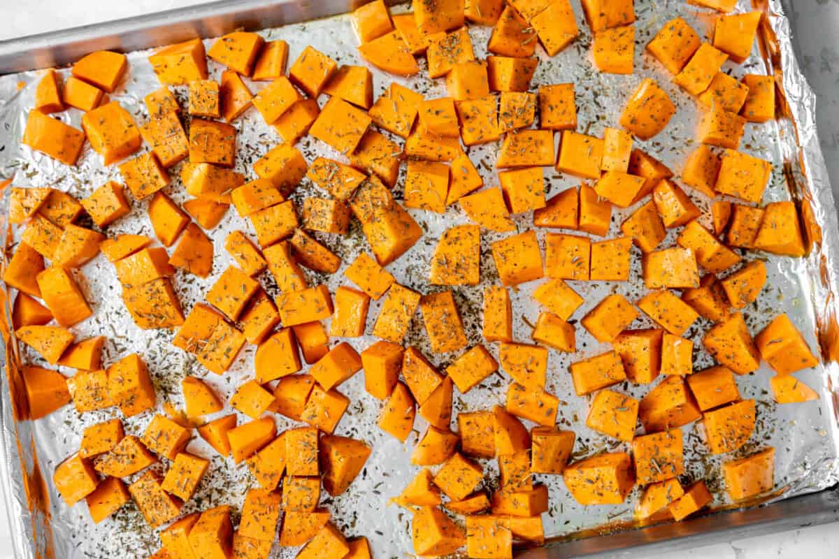 Sweet potatoes coated in olive oil, salt, and dried herbs, spread out in an even layer on a baking sheet. 