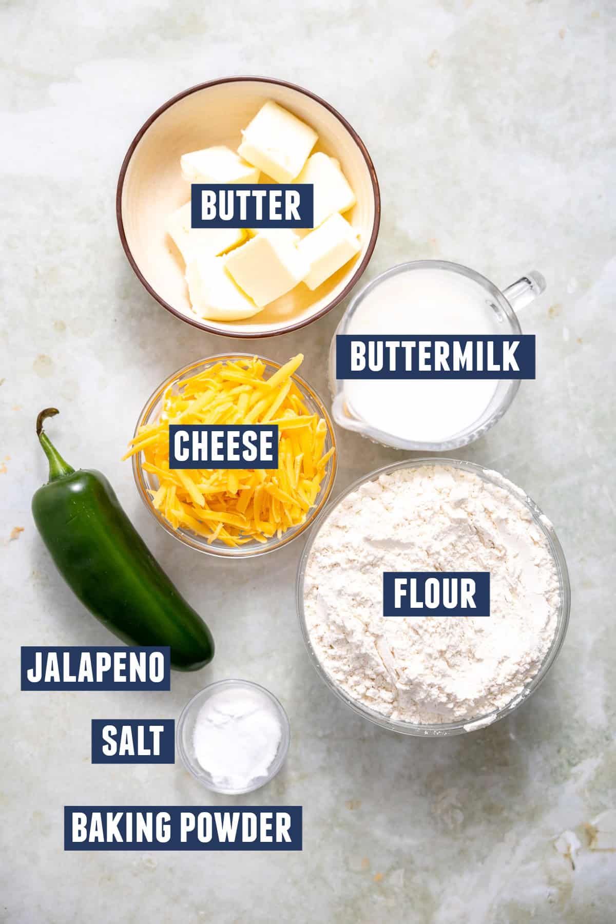 Ingredients needed to make Jalapeño Cheese Biscuits. Including: flour, butter, baking powder, salt, buttermilk, cheese, and jalapeño.