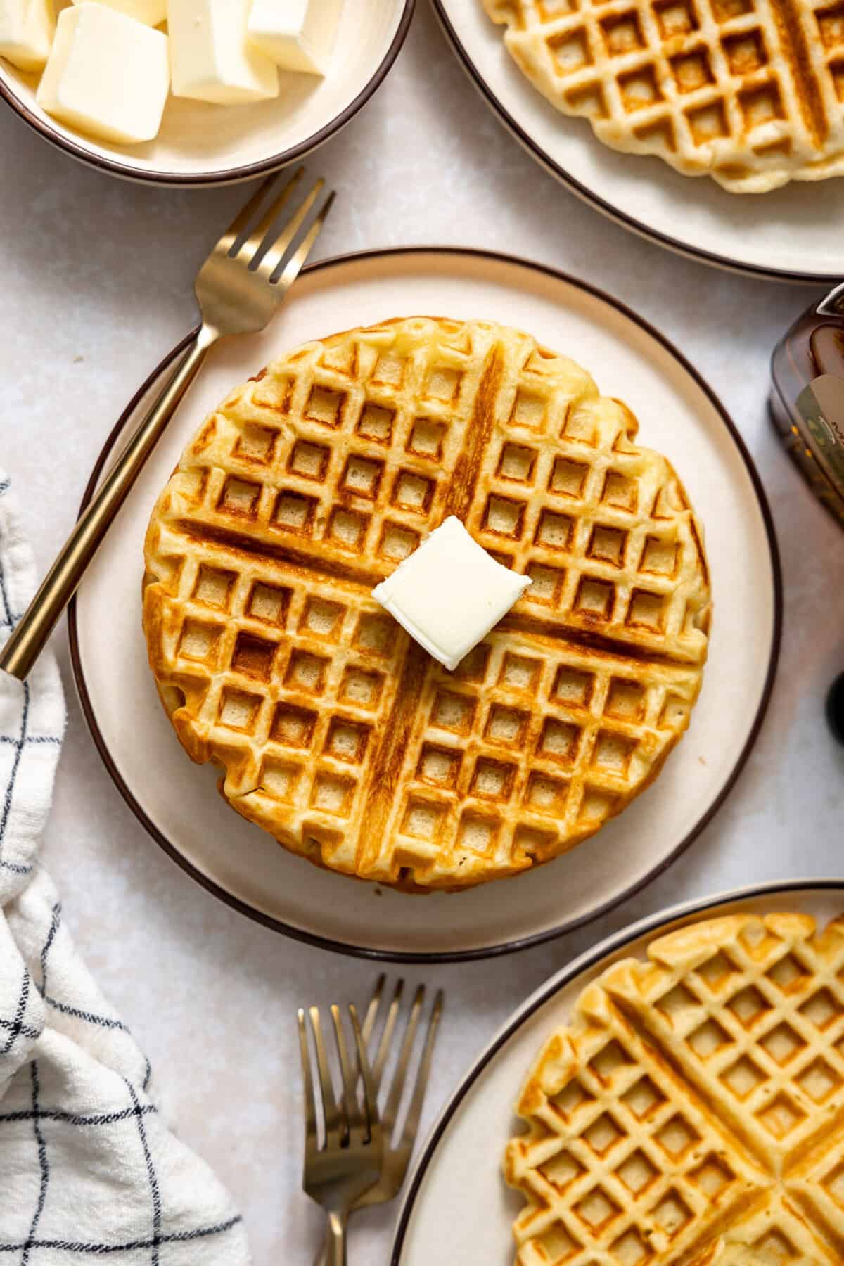 Overhead view of waffles on plates with butter. 