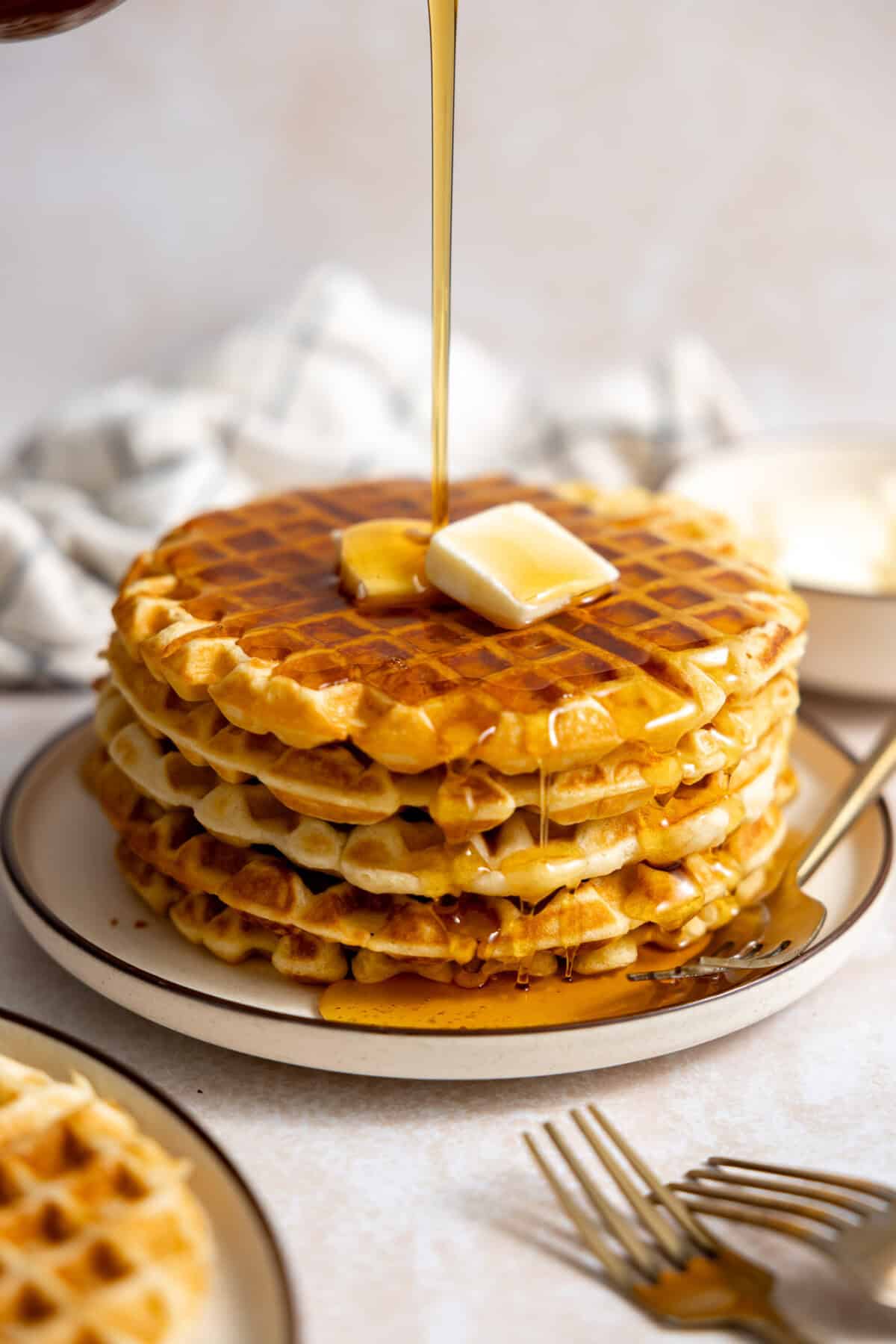 Stack of buttermilk waffles with butter on top and syrup drizzling over. 