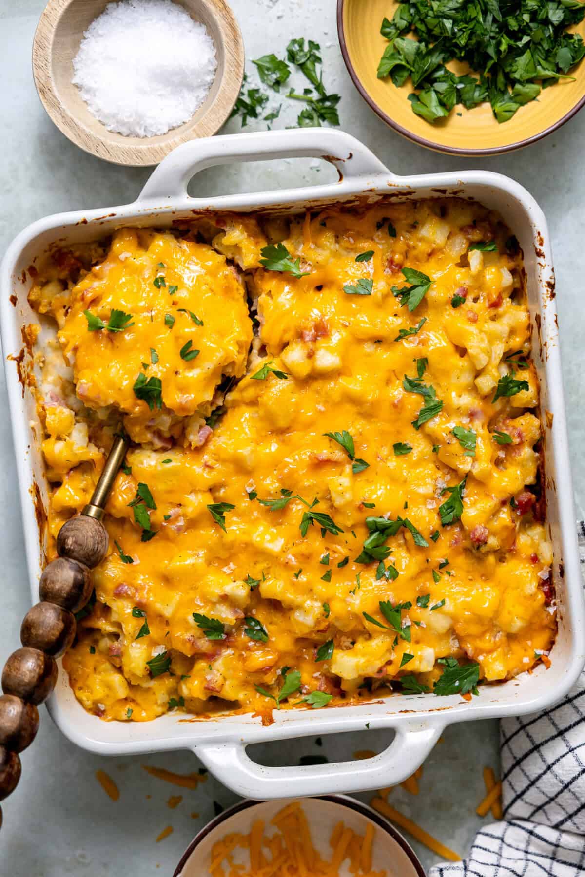 Ham and potato casserole in a white baking dish with a wooden serving spoon.