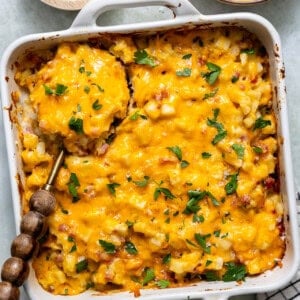 Ham and potato casserole in a white baking dish with a wooden serving spoon.