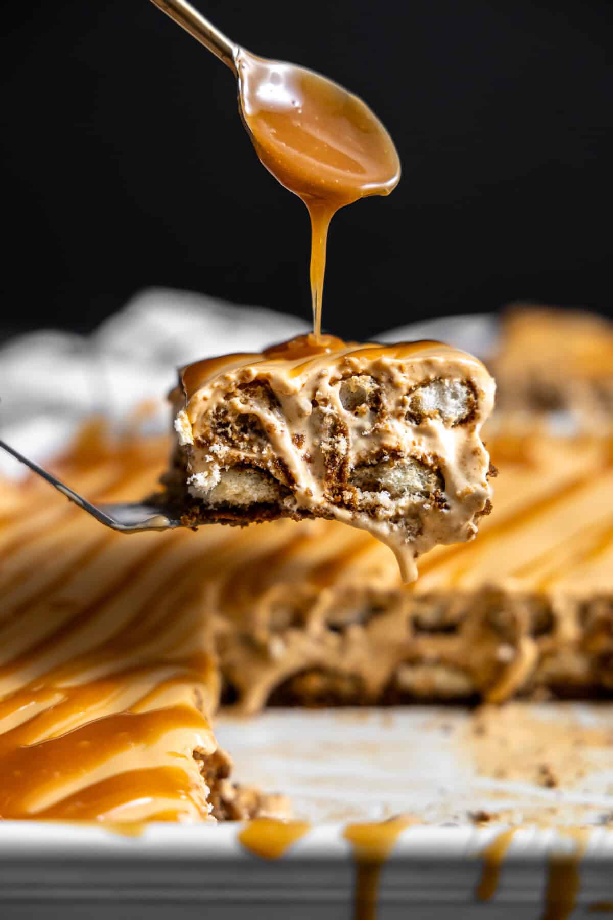 Slice of dulce de leche tiramisu being drizzled with caramel sauce on top. 