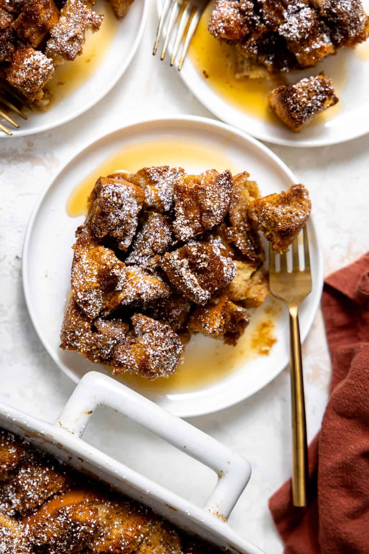 French toast casserole served on a white plate and drizzled with maple syrup. 