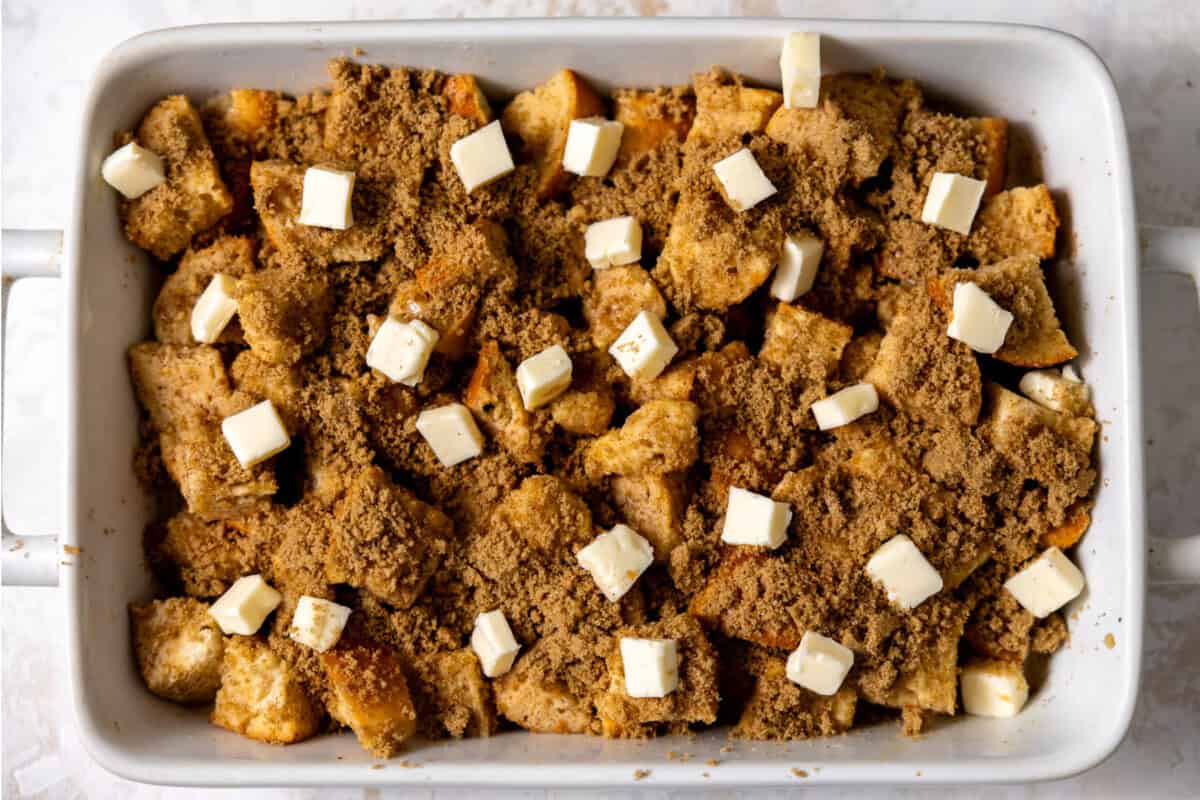 French toast casserole with French bread cubed, custard poured over, sugar cinnamon topping and butter cubed up ready for baking. 