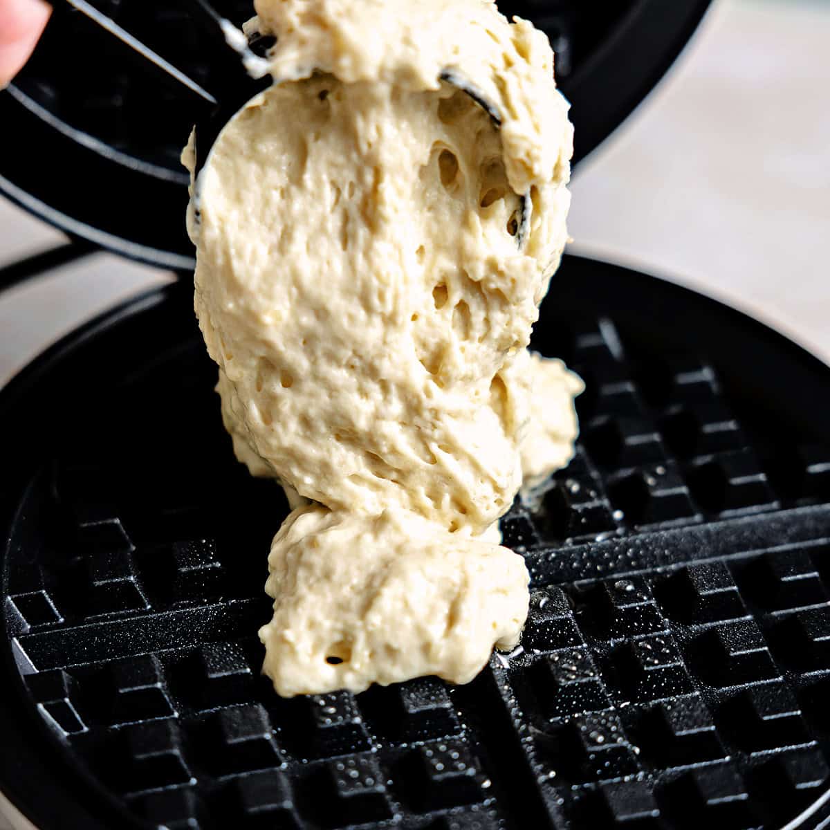 Waffle batter being spooned onto a waffle iron for cooking. 