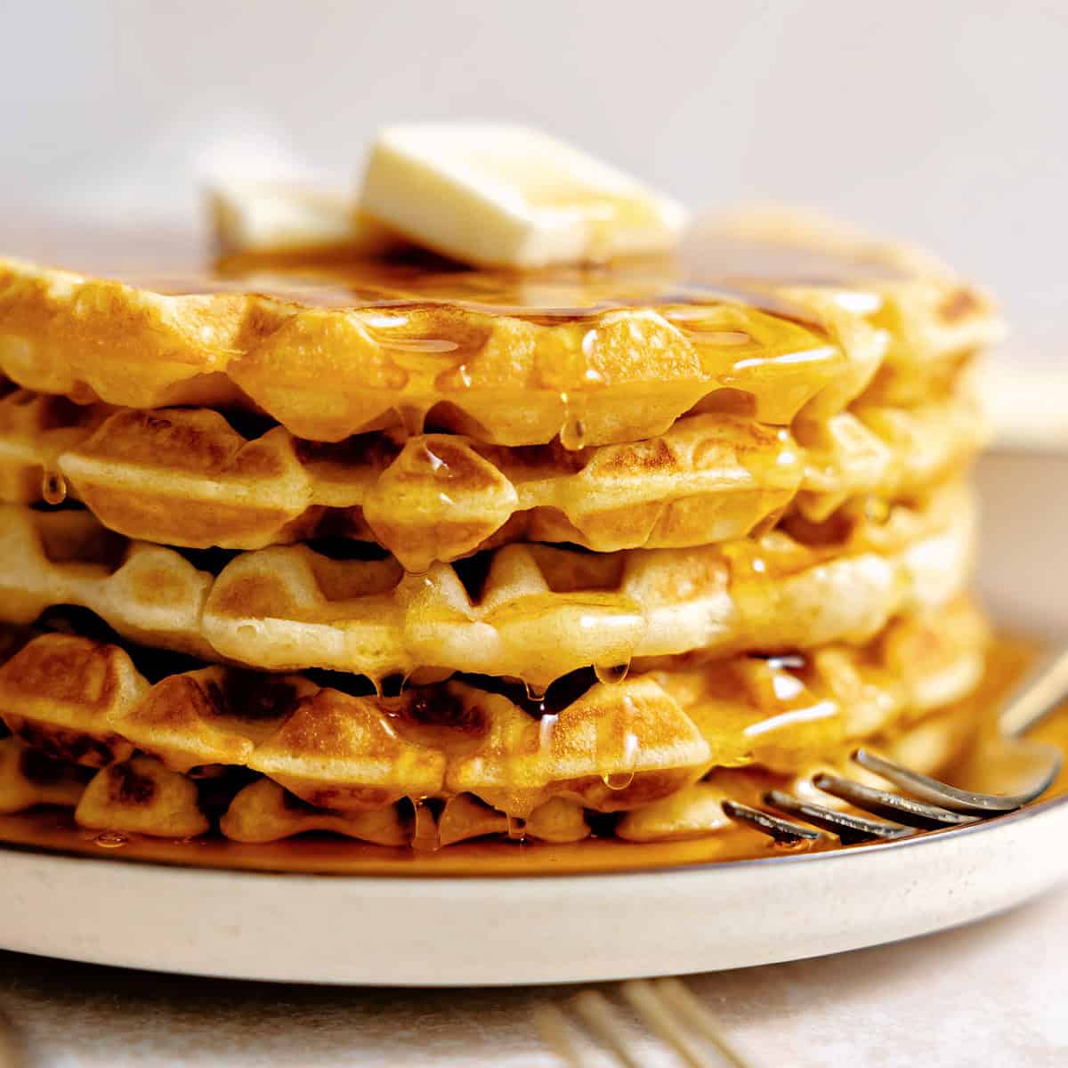 Stack of buttermilk waffles with syrup and butter. 