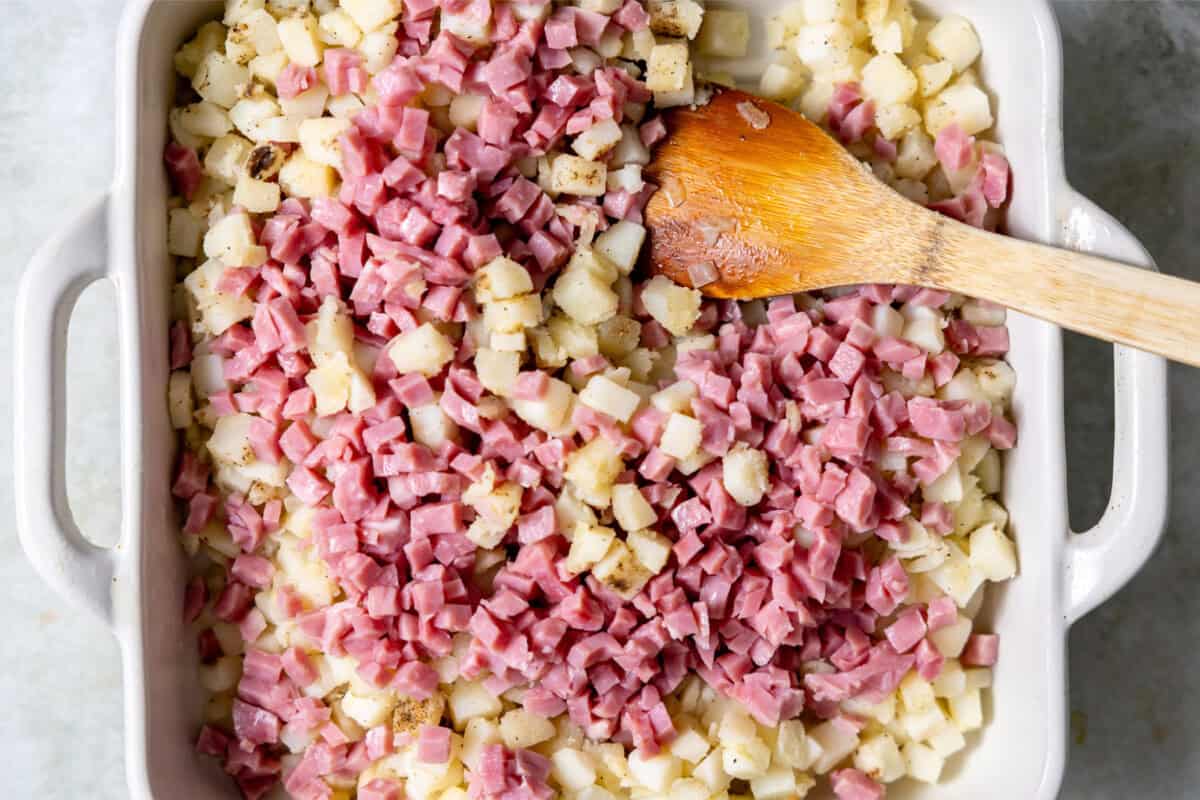 Ham and potato being stirred together in a baking dish. 