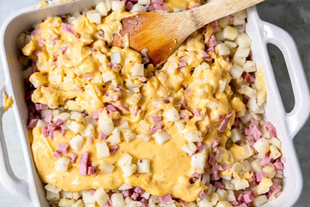 Cheese sauce poured over ham and potatoes in a baking dish. 