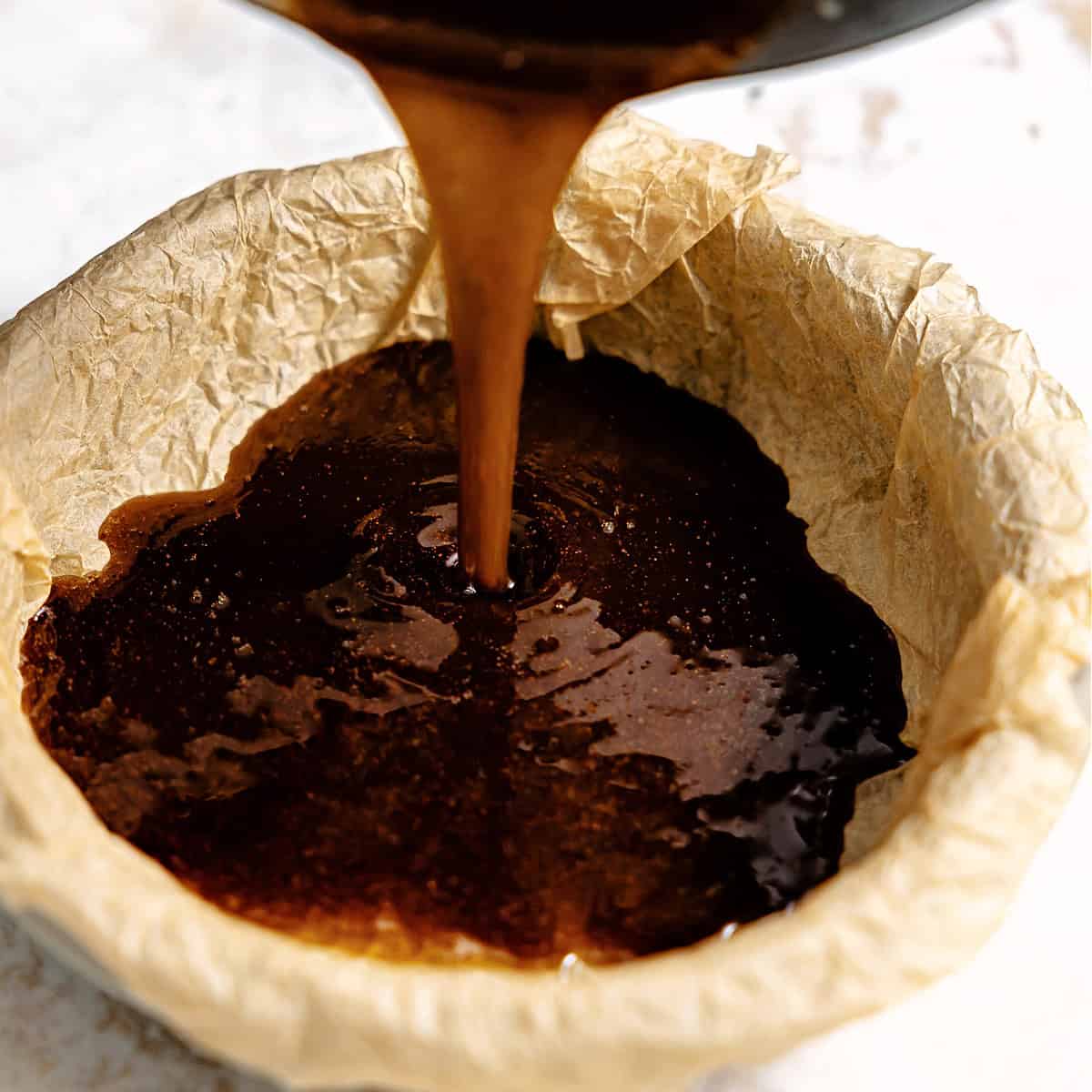 Pouring butter and brown sugar mixture into a parchment lined baking dish.