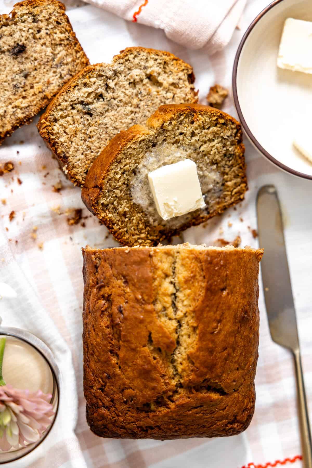 Loaf of banana bread being sliced and served with butter. 