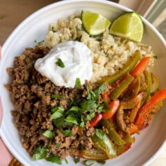 Ground beef fajita bowls with veggies, rice, sour cream, and lime wedges. 