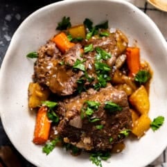 Bowl with pot roast, carrots, and potatoes all garnished with fresh parsley.