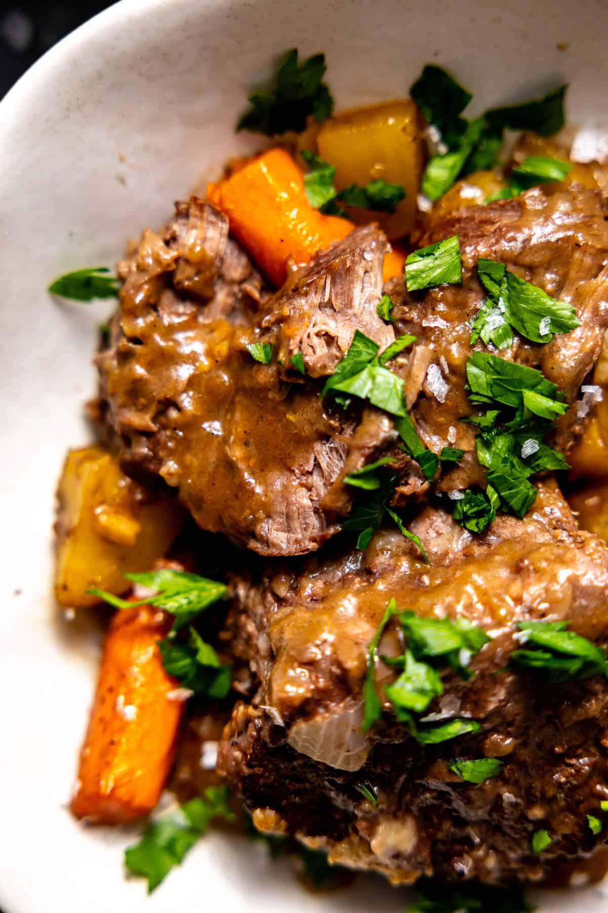 Cooked pot roast topped with parsley, served with carrots and potatoes. 